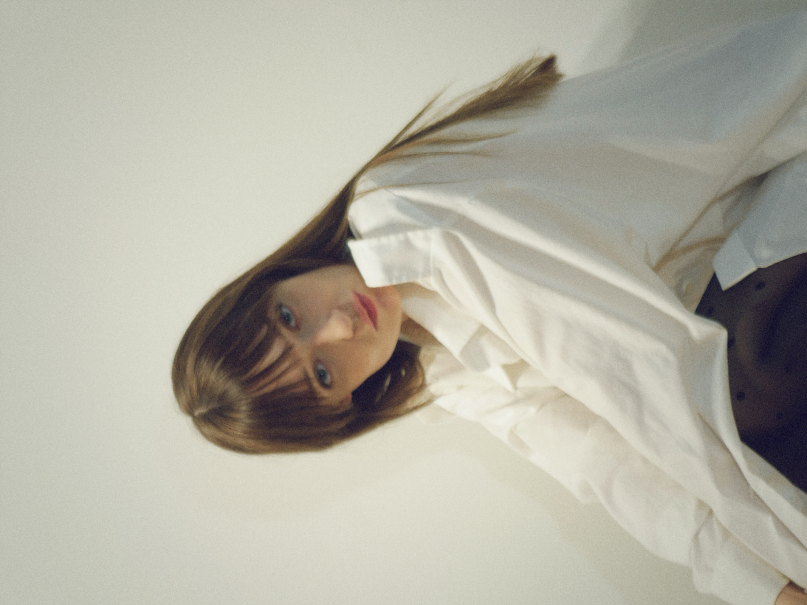 Kris Brouillette seated in an oversized white shirt, leaning forward and looking into the camera